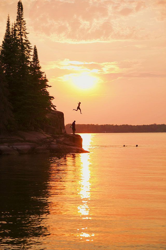 a person jumping into the water from a rock outcropping in front of a sunset