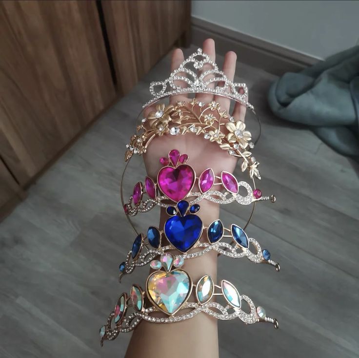 a woman's hand holding several bracelets with hearts and jewels on them, all in different colors