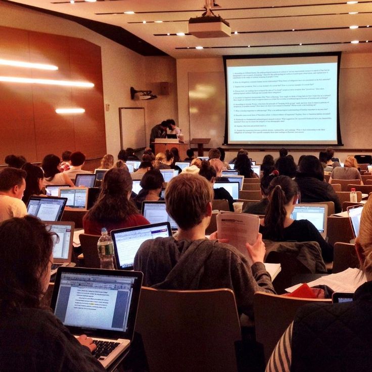 a classroom full of students with laptops and projector screen in the back ground