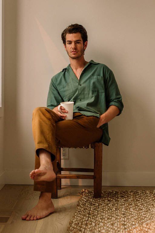 a man sitting in a chair with his feet up and holding a coffee cup while looking at the camera