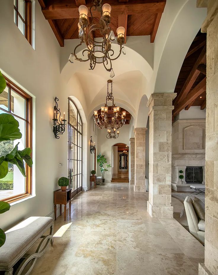 a large hallway with chandeliers and windows on both sides of the hall, leading to an open living area