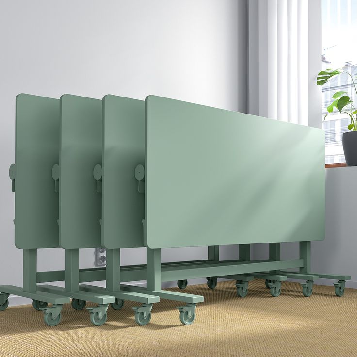 three green partitions sitting next to each other on wheels in front of a window