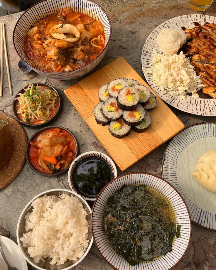 several plates of food on a table with chopsticks, rice and other foods