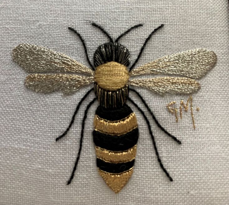 a close up of a bee embroidered on a piece of white fabric with gold and black details