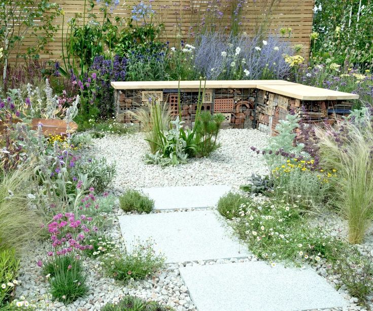 a garden with various types of flowers and plants around it, including an outdoor bench