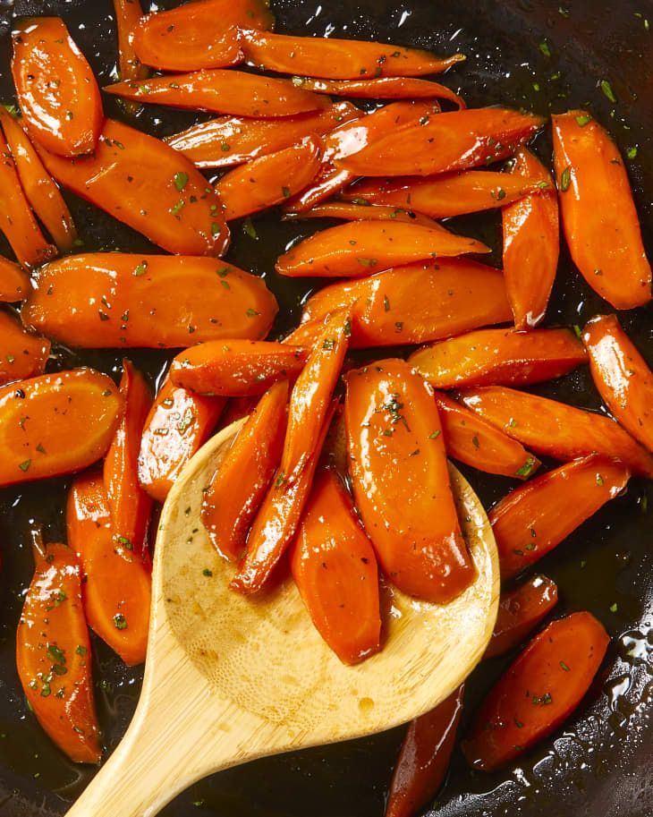 carrots being cooked in a pan with a wooden spoon