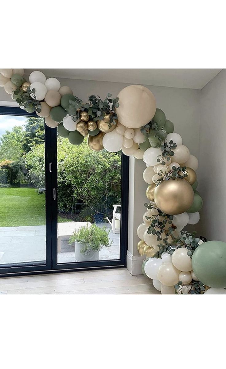 a balloon arch with gold, white and green balloons hanging from it's sides