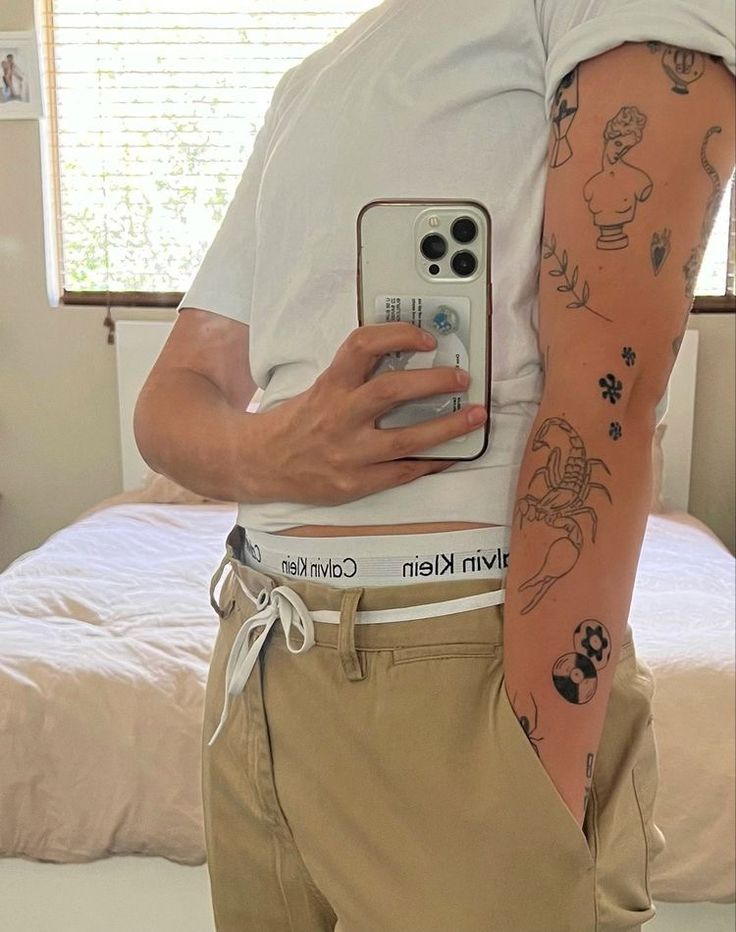 a man with tattoos on his arm holding a cell phone in front of his stomach