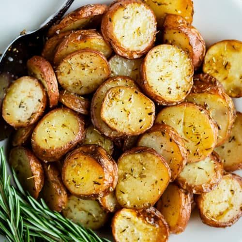 a white plate topped with sliced potatoes and rosemary garnish next to a fork