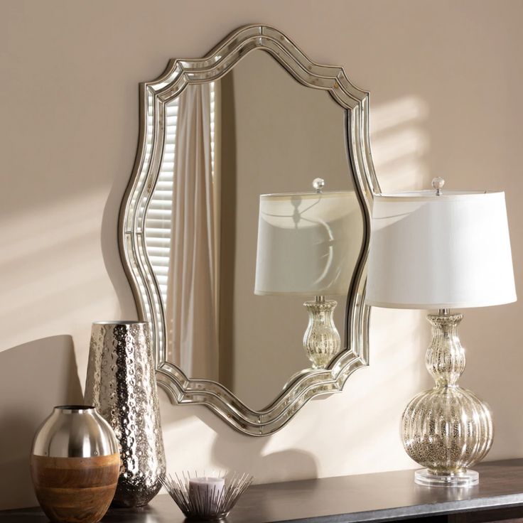 a mirror sitting on top of a wooden table next to a lamp and vases