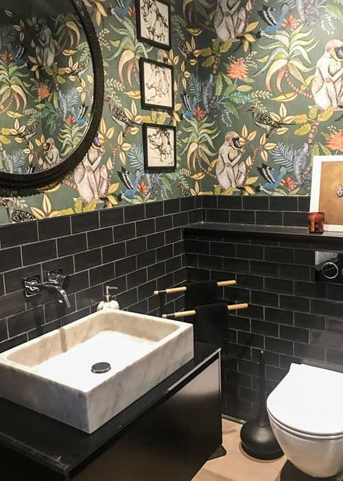 a bathroom with black tile and floral wallpaper on the walls, along with a white toilet and sink