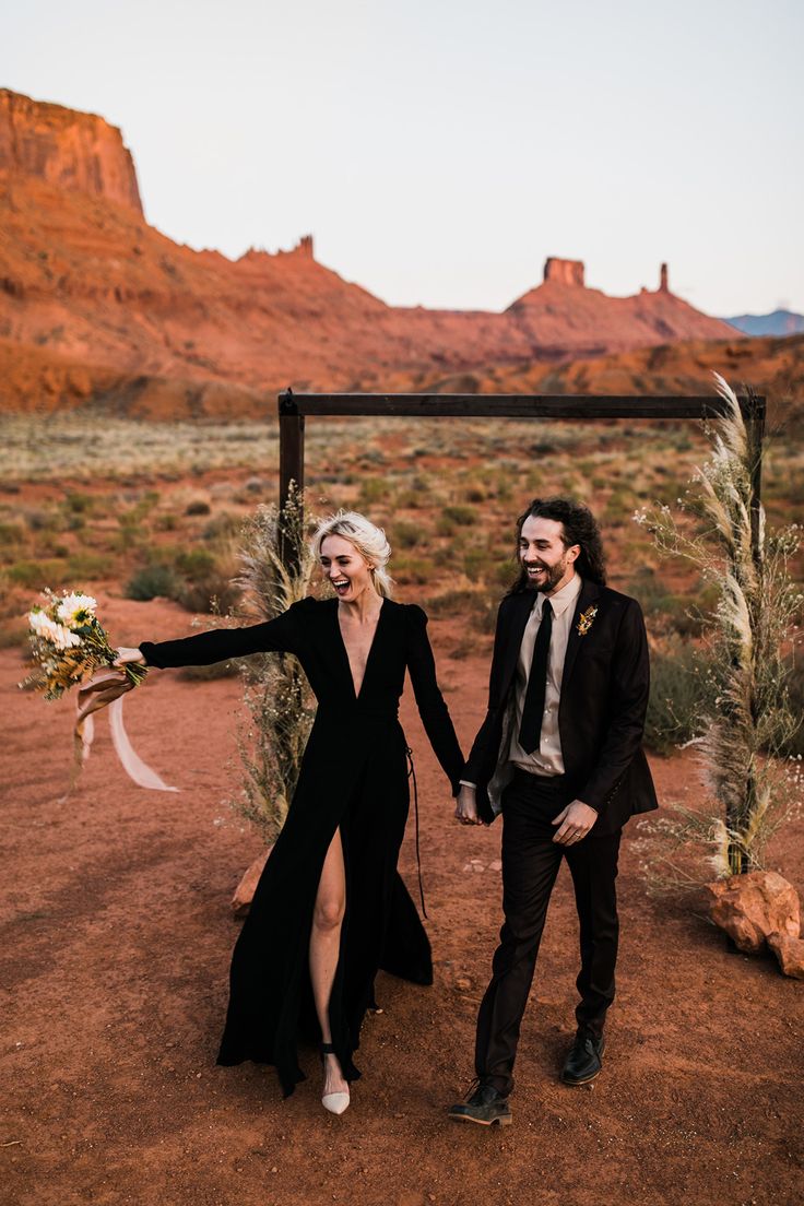 a man and woman walking down a dirt road in front of a desert landscape with mountains