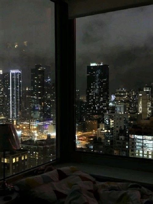 a view of the city at night from a bedroom in a high rise apartment building