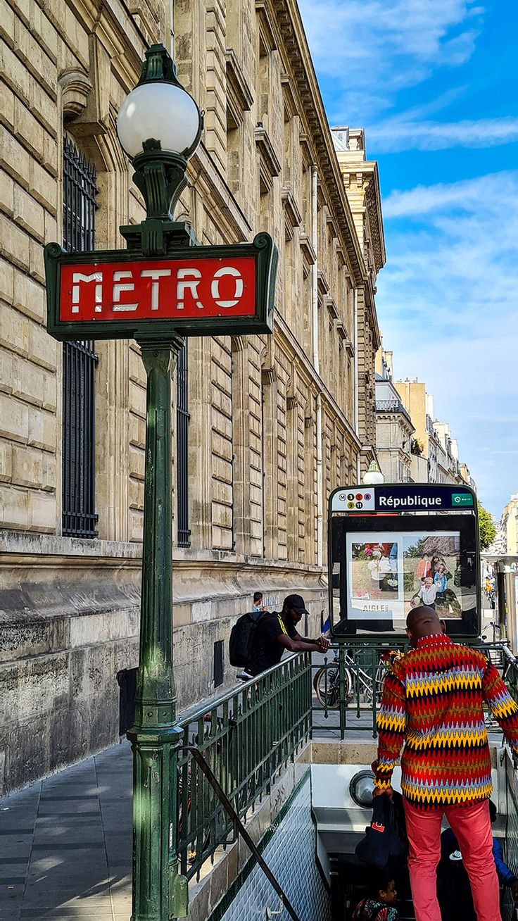 a man standing next to a street sign in front of a tall building with a red metro sign on it's side