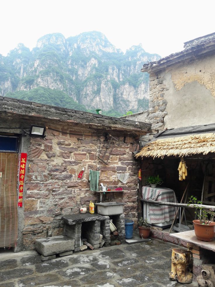 an old stone building with mountains in the backgroud and potted plants outside