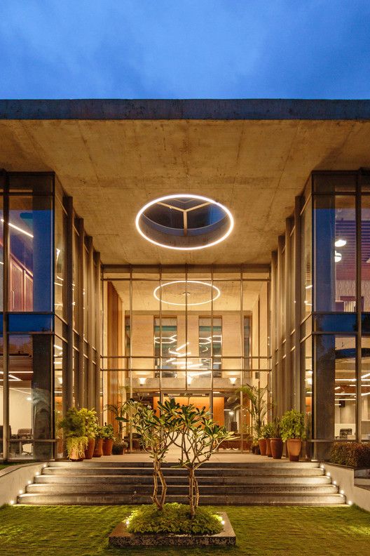 the entrance to a modern building with plants and lights on it's sides at night