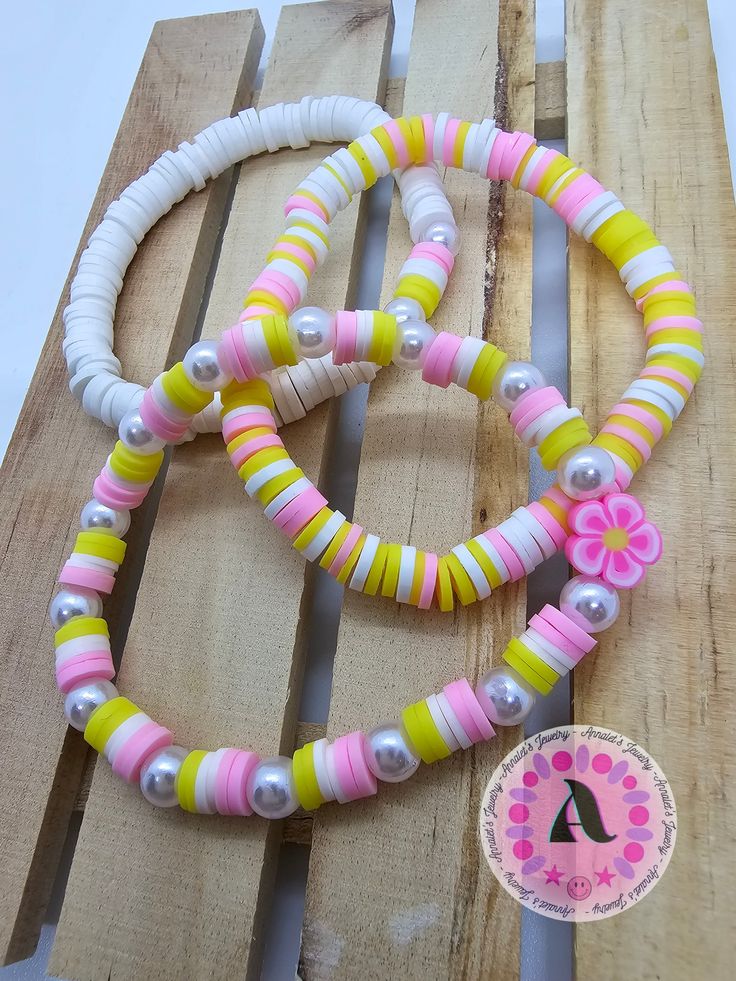 two bracelets are sitting on top of a piece of wood with beads and flowers