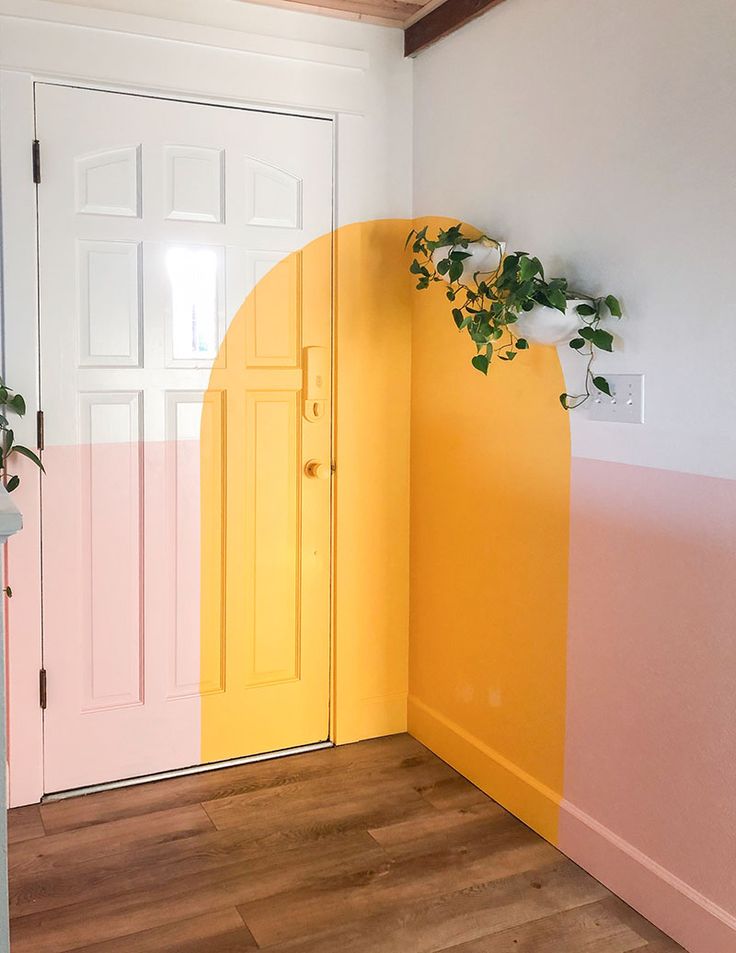 a yellow door with pink and white paint on the wall next to a potted plant