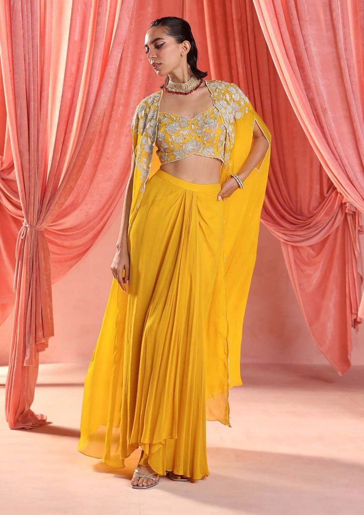 Dazzle in this enchanting ensemble: an embellished choli paired seamlessly with an embellished cape, adding a touch of drama and elegance. Complete the look with a draped skirt for effortless grace and sophistication, perfect for any glamorous affair. Yellow Dhoti Dress For Haldi Function, Fitted Dress With Cape Sleeves For Navratri, Diwali Draped Sets With Dupatta, Navratri Palazzo Set With Zari Work And Cape Sleeves, Bollywood Draped Sets For Navratri, Festival Palazzo Set With Dupatta And Cape Sleeves, Festive Draped Sharara With Sheer Dupatta, Festive Draped Lehenga With Resham Embroidery, Festive Palazzo Set With Cape Sleeves For Navratri