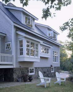 two lawn chairs sitting in front of a house with large windows on the second floor