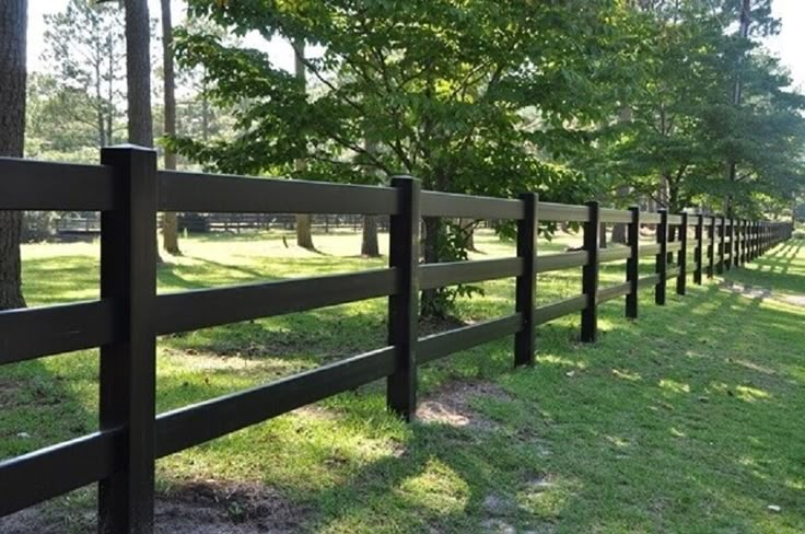 a wooden fence in the middle of a grassy field with trees and grass on both sides