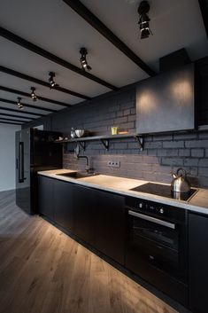 an empty kitchen with black cabinets and wood flooring on the walls is lit by recessed lighting