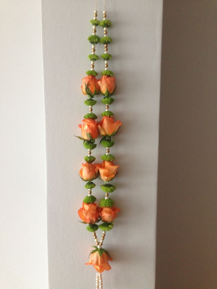 an orange flower is hanging on the wall next to a beaded necklace with pearls