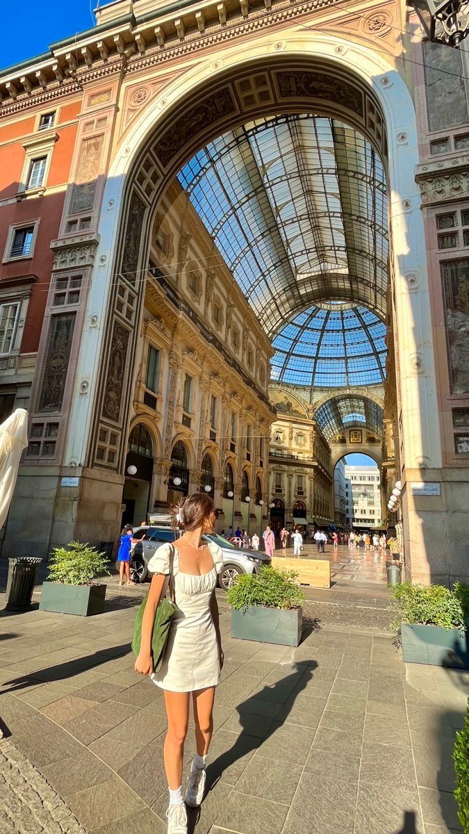 a woman is walking down the street in front of a building with a glass roof