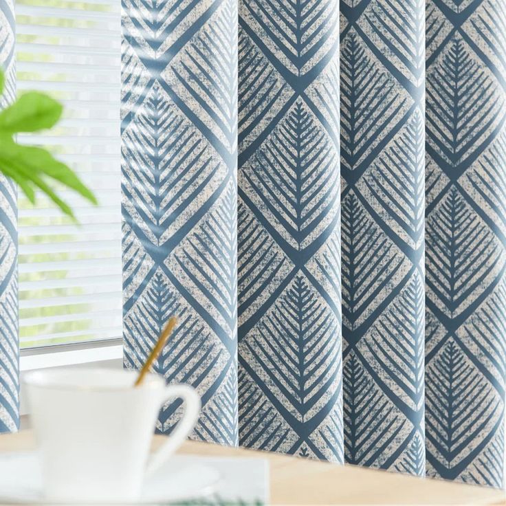 a coffee cup sitting on top of a table next to a window covered in blue and white curtains