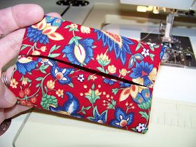 a person is using a sewing machine to sew a red flowered fabric wallet