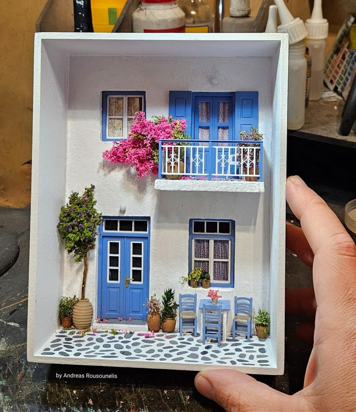 a hand holding up a miniature model of a house with blue shutters and balconies