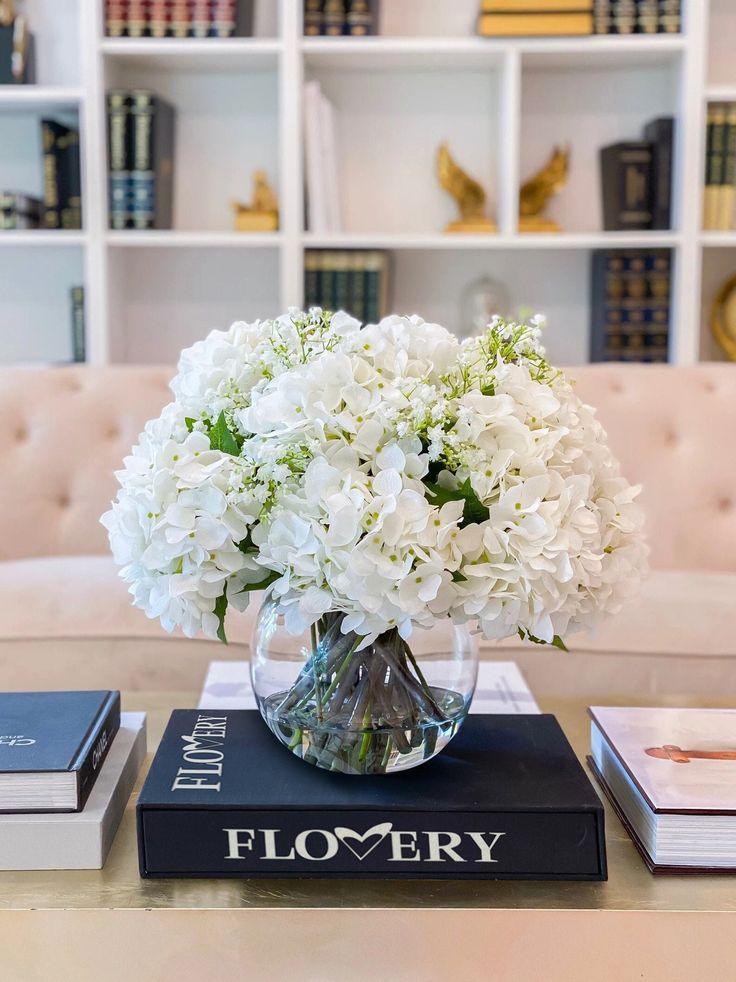 a vase filled with white flowers sitting on top of a book next to a couch