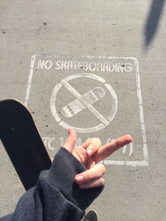 a person pointing at a no skateboarding sign on the ground with their finger in the air