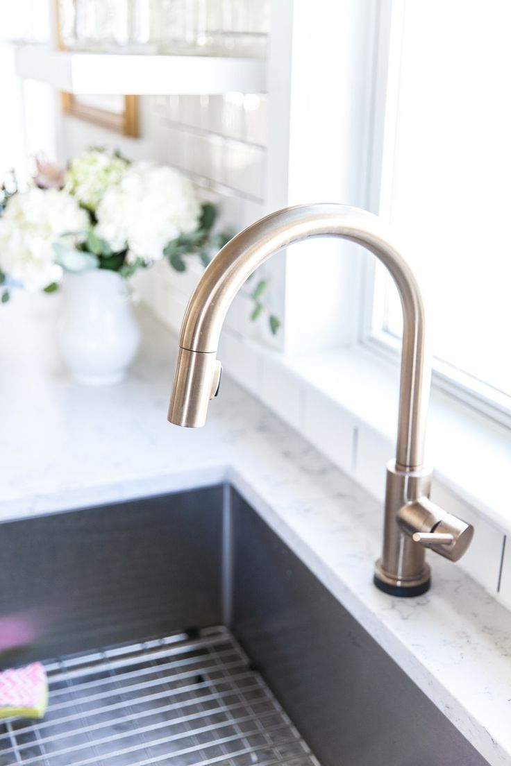 a stainless steel sink in a white kitchen with flowers on the window sill behind it