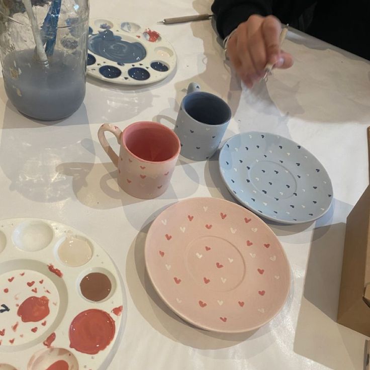 the table is set with plates, cups and utensils to paint hearts on