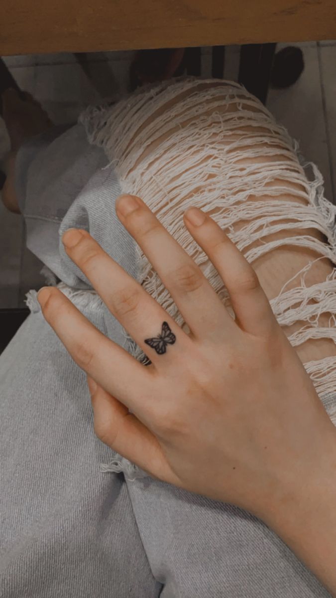 a woman's hand with a small butterfly tattoo on her left index finger, resting on a pillow