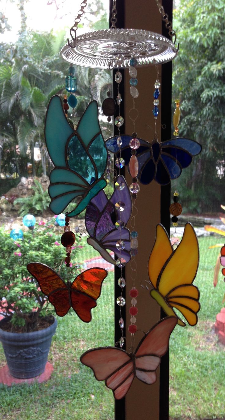 several colorful glass butterflies hanging from a pole in front of a window with potted plants