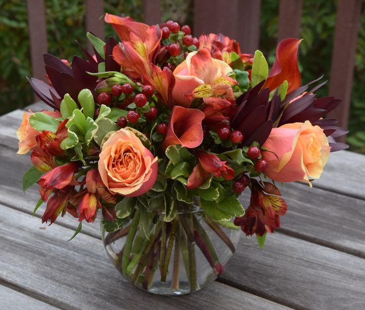 a vase filled with orange and red flowers on top of a wooden table next to a fence