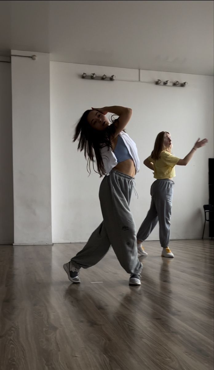 two young women are dancing in an empty room with wood flooring and white walls