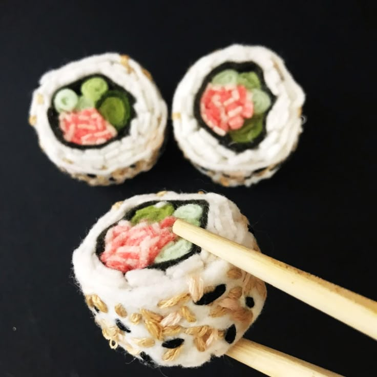 three sushi rolls with chopsticks on a black surface, one is decorated with flowers and leaves