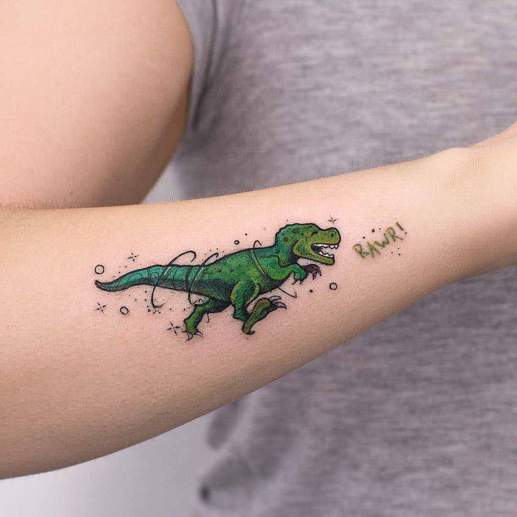 a woman's arm with a small green dinosaur tattoo on the left side of her arm