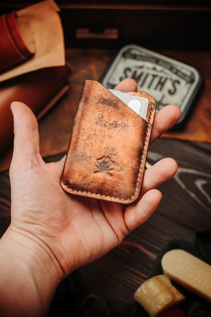 a hand holding an old leather wallet in front of some other items on a table