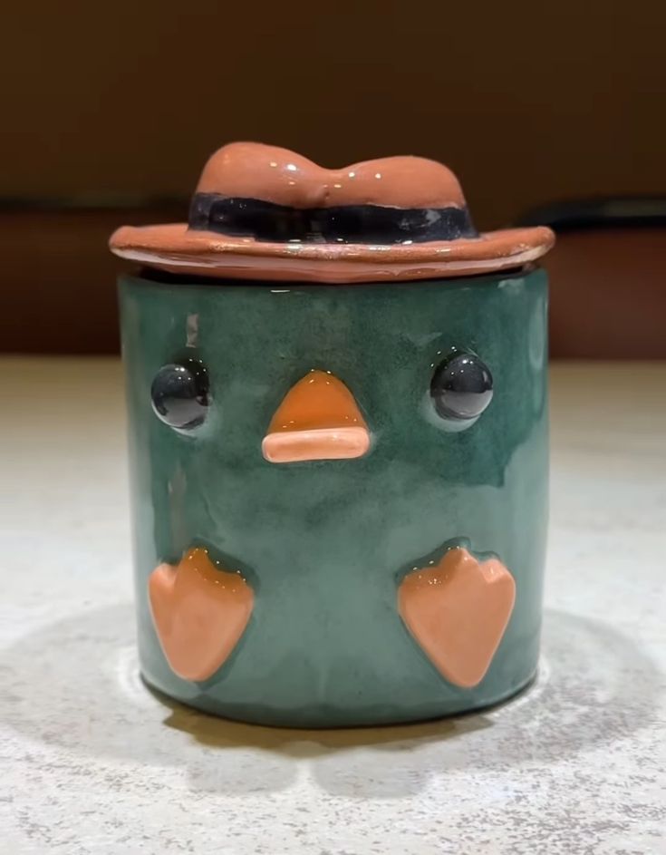 a ceramic bird with a hat on its head sitting on a counter top next to a wall