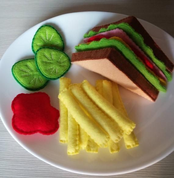 a white plate topped with sandwiches and pickles on top of a wooden table next to a green leaf