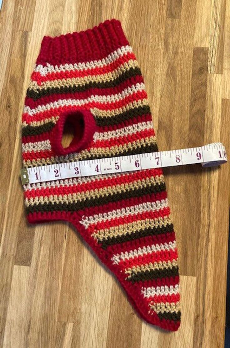 a red and black striped knitted mitt next to a measuring tape on the floor