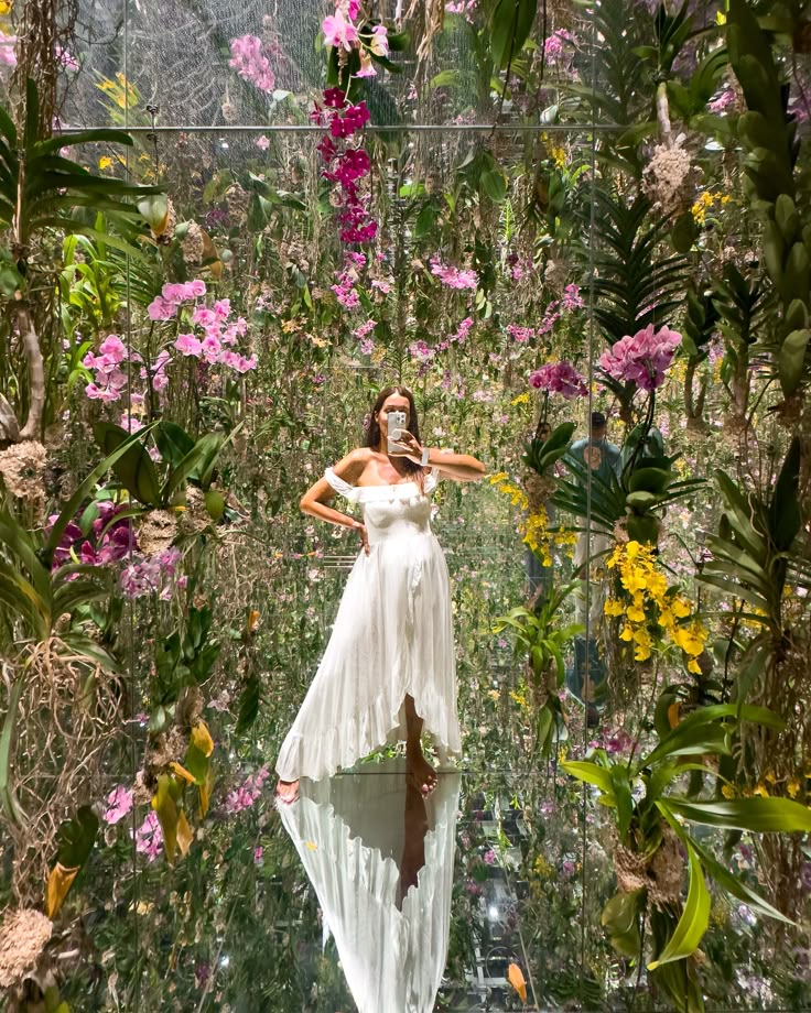 a woman in a white dress is standing on a bridge surrounded by plants and flowers