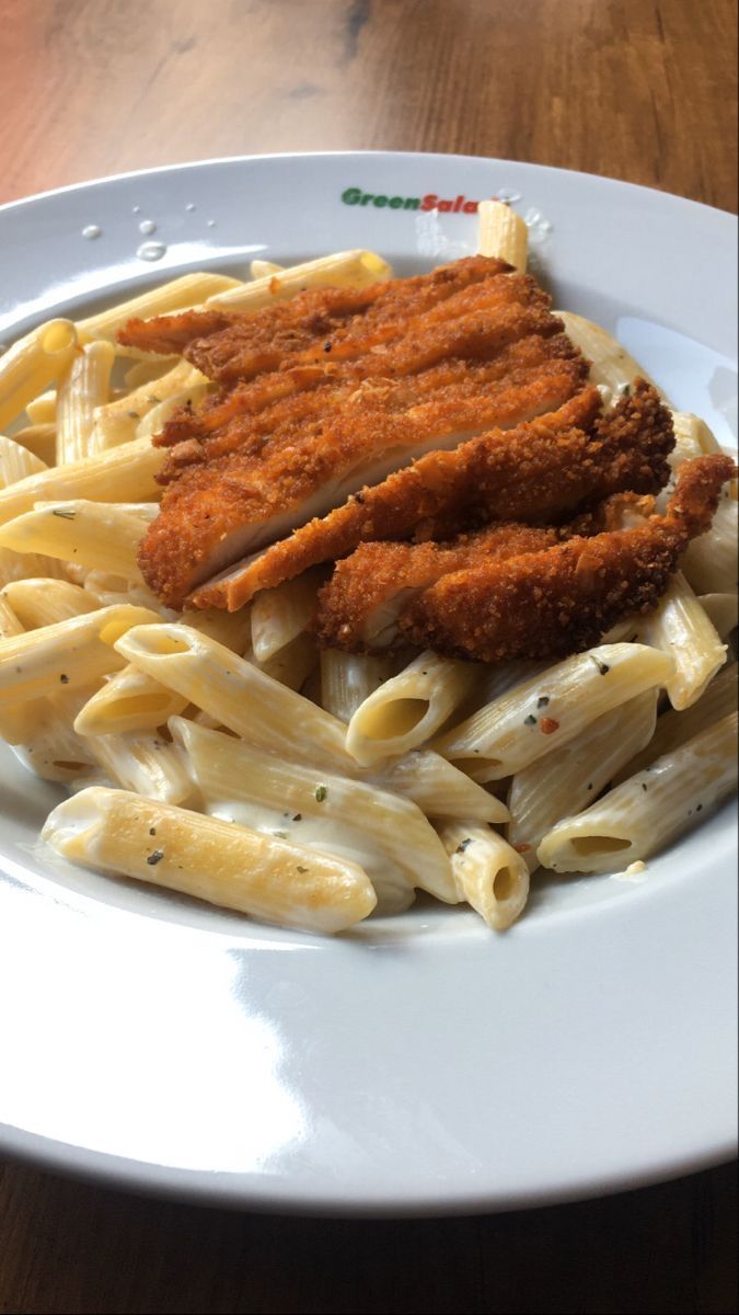 a plate with pasta, chicken and sauce on it sitting on top of a wooden table