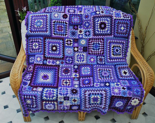 a crocheted blanket sitting on top of a wicker chair next to a window