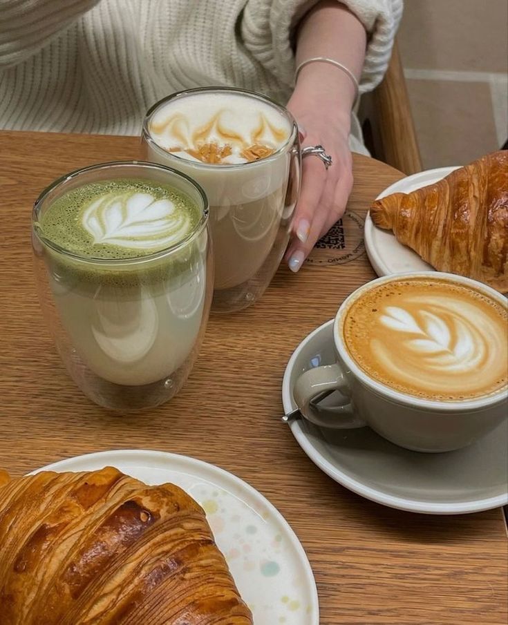 there is a croissant and two cups of coffee next to each other on the table