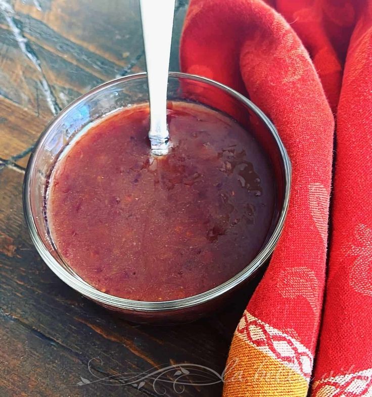 a glass bowl filled with red liquid on top of a wooden table next to two napkins